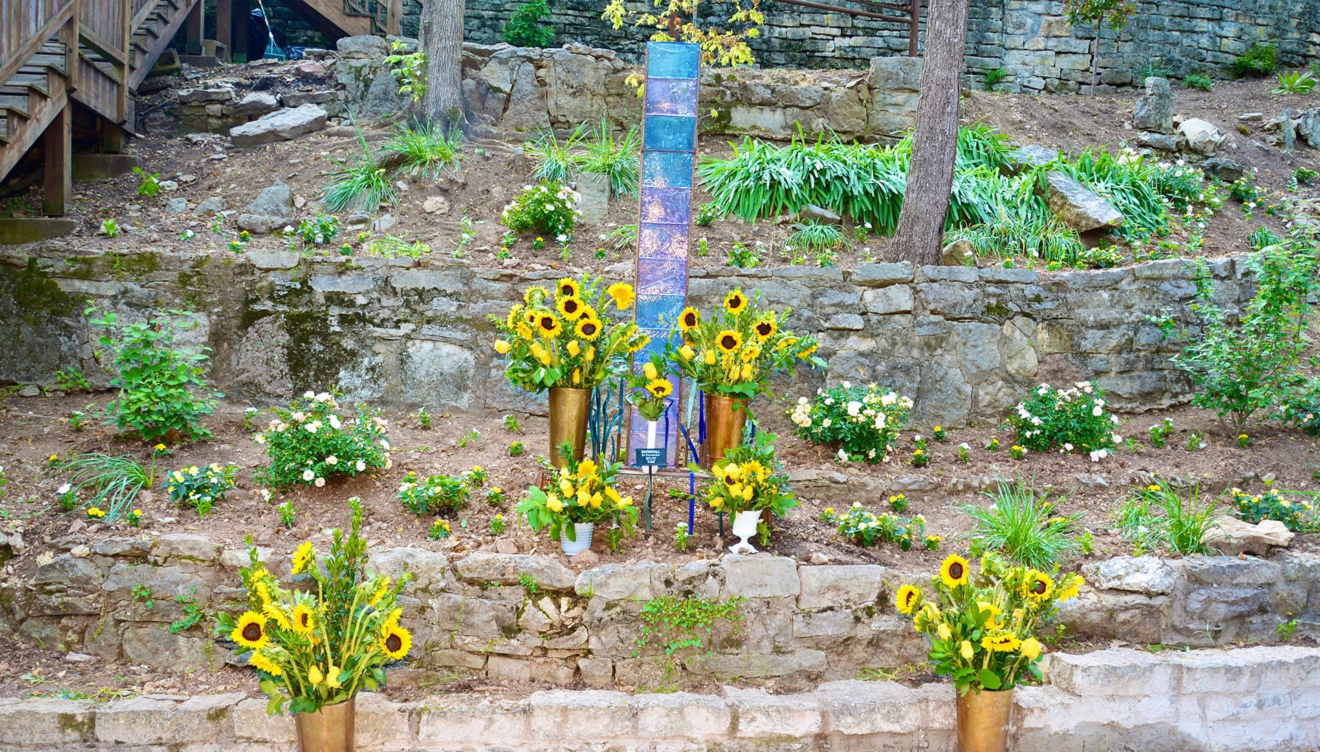 A stone garden displays vibrant arrangements of sunflowers surrounded by lush greenery.