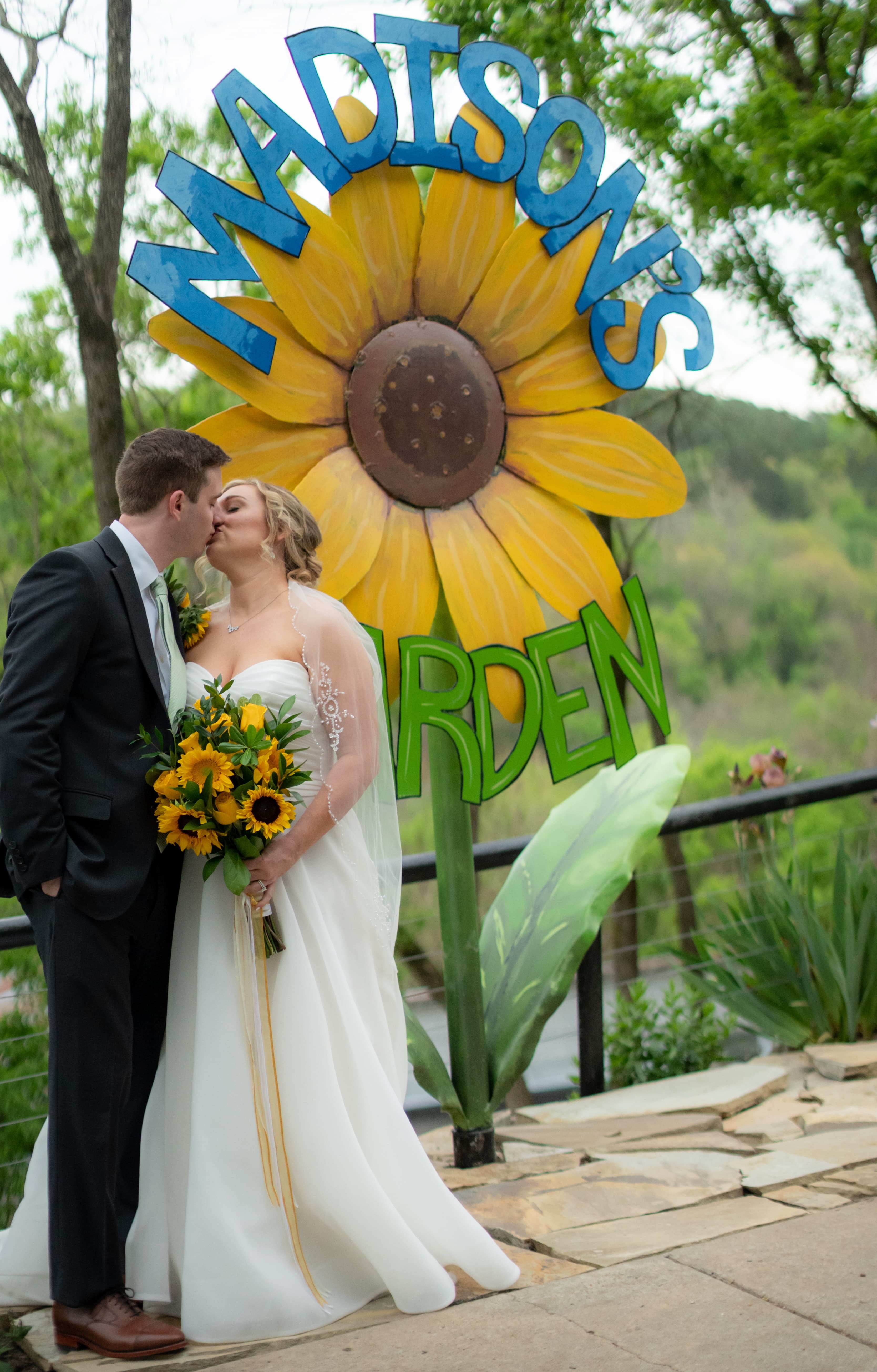 A newlywed couple kisses in front of a vibrant sunflower mural at "Madison's Garden."