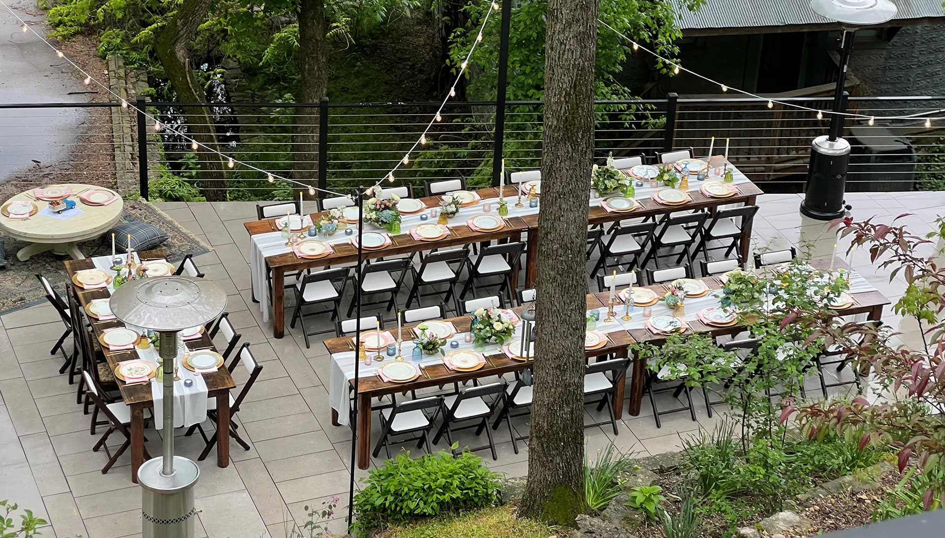An outdoor dining setup featuring long wooden tables adorned with plants and tableware.